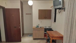 A compact kitchen with a wooden cabinet, a small table, and a television mounted on the wall. - Rousetis Studio 201 - 200m from the Sea in Aígio (Aigialeia)