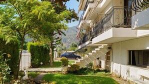 Um edifício residencial com jardim, um carro estacionado na frente e uma escadaria que leva à entrada.