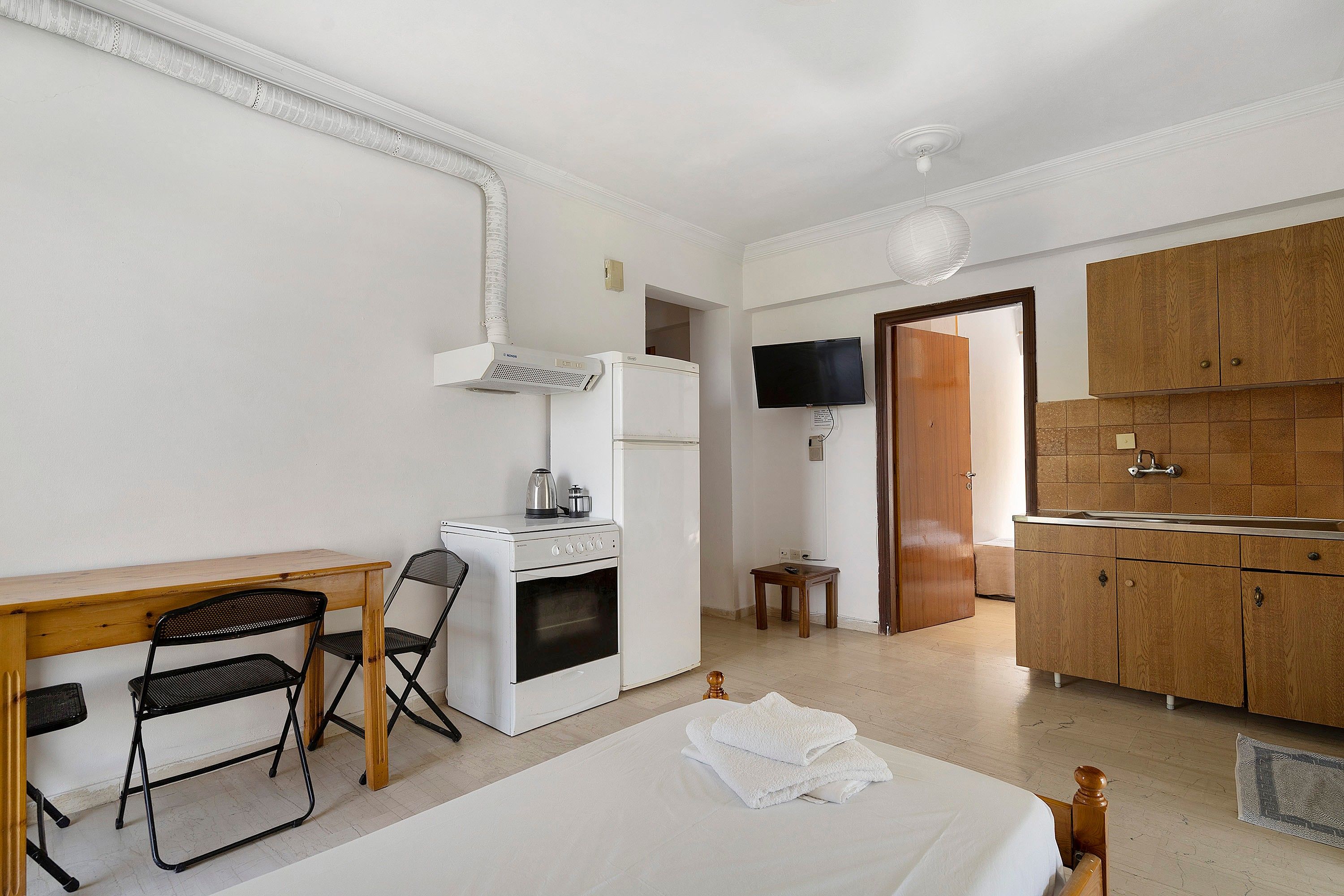 Une chambre d’hôtel compacte comprenant un lit, une petite kitchenette, un coin repas avec une table et des chaises, et un téléviseur fixé au mur.