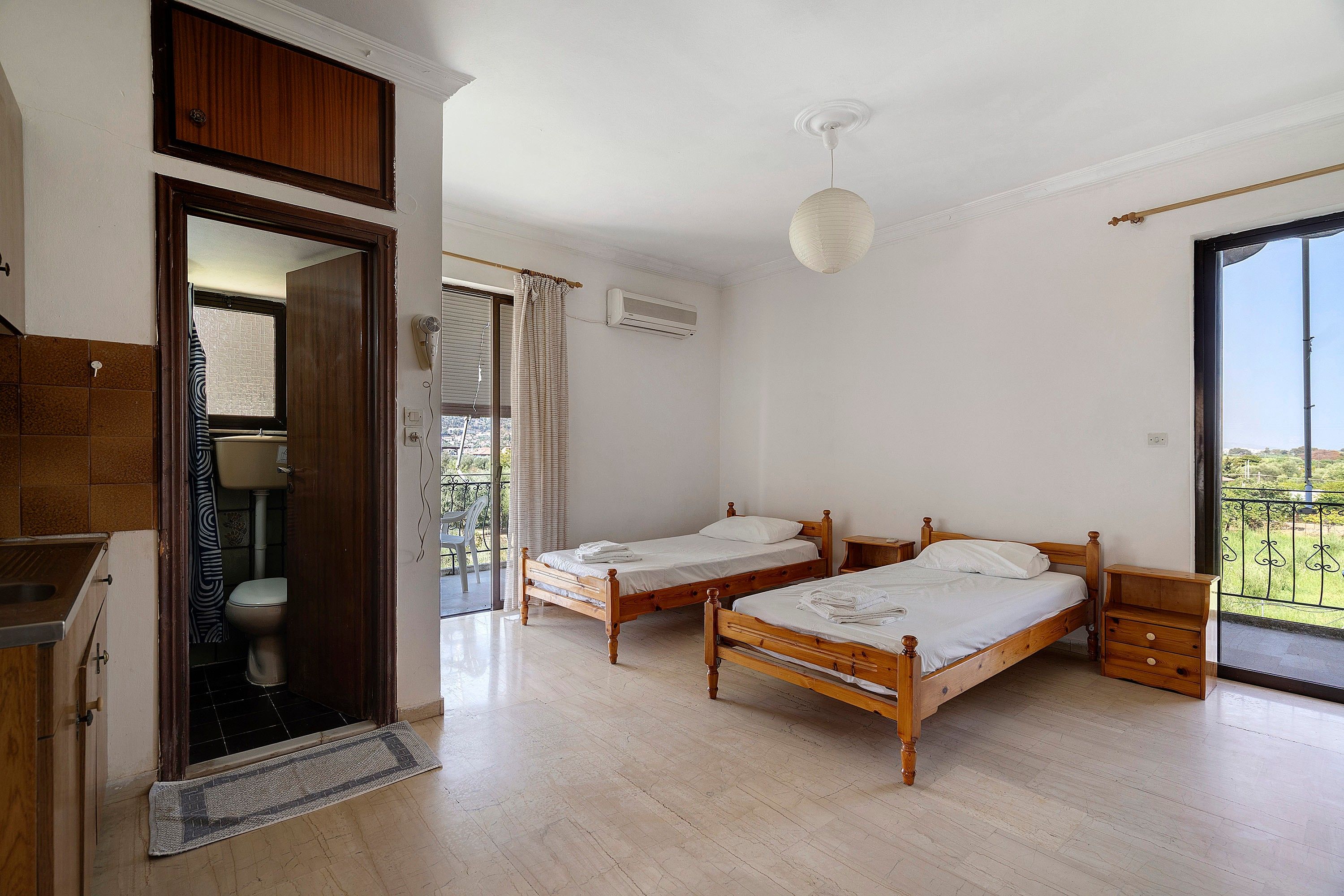 A bedroom with two wooden beds, a bathroom with a toilet and sink, and a balcony with a view.
