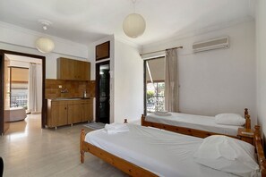 A bedroom with two single beds, a kitchenette, and a bathroom. - Rousetis Two-Bedroom Apt 202 - 200m from the Sea (Aigialeia)