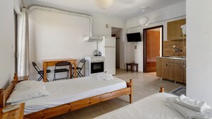 Quarto com cama, escrivaninha, cadeira, televisão e cozinha compacta.