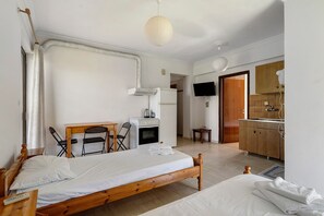 Ein Zimmer mit Bett, Schreibtisch, Stuhl, Fernseher und einer Küchenzeile.