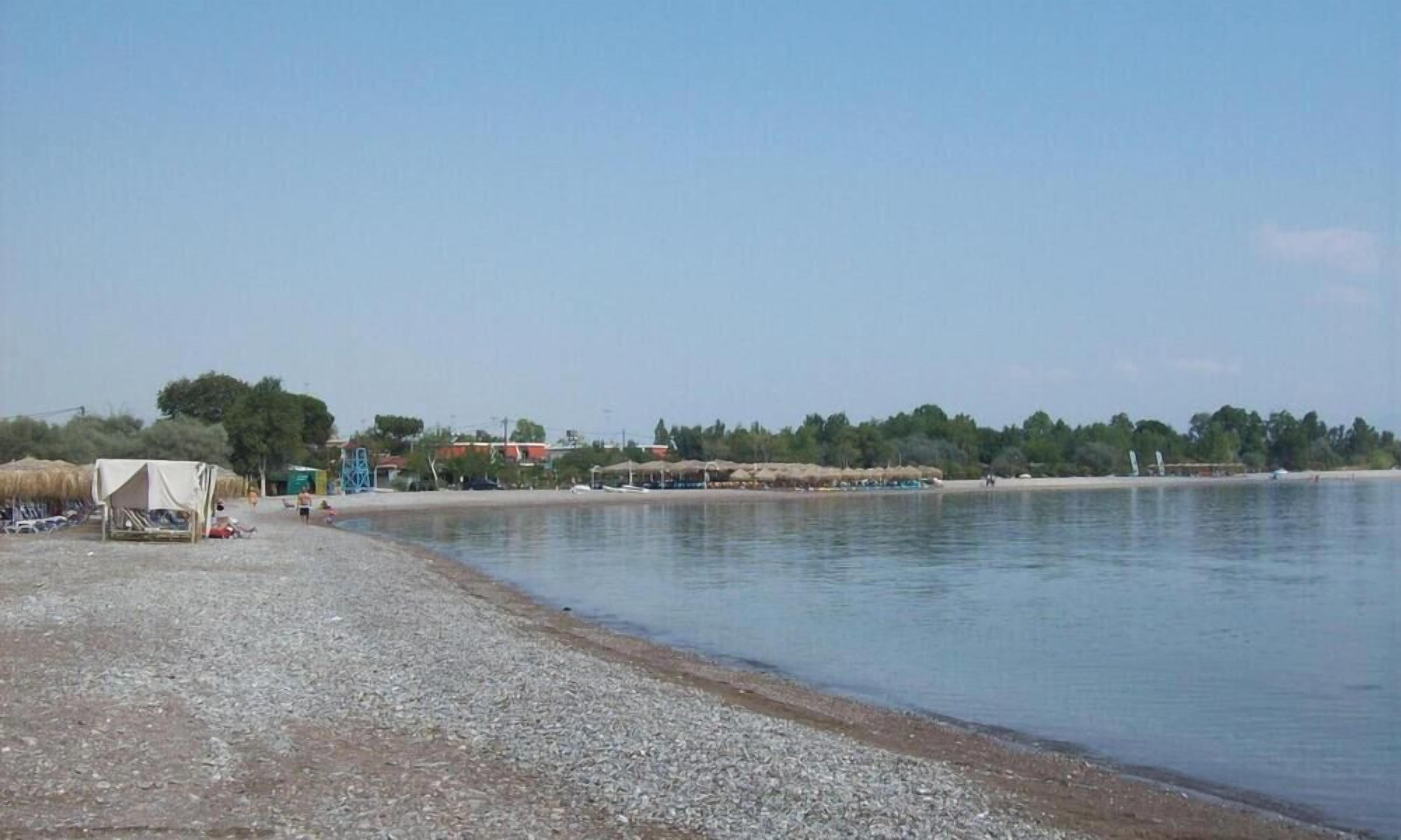 A beach with a pebbly shore, a few tents, and a calm water body.