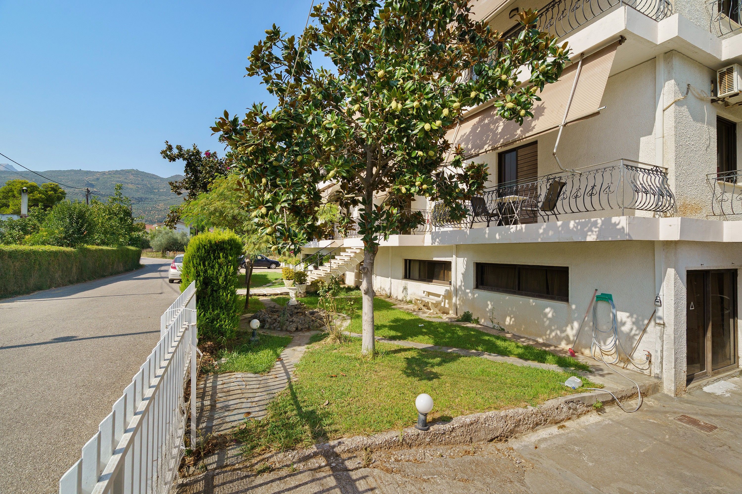 A residential building with a balcony, a paved driveway, and a clear sky.