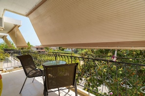 Ein Balkon mit Tisch und Stühlen, einem Metallgeländer und Blick auf Grünflächen sowie Gebäude im Hintergrund.
