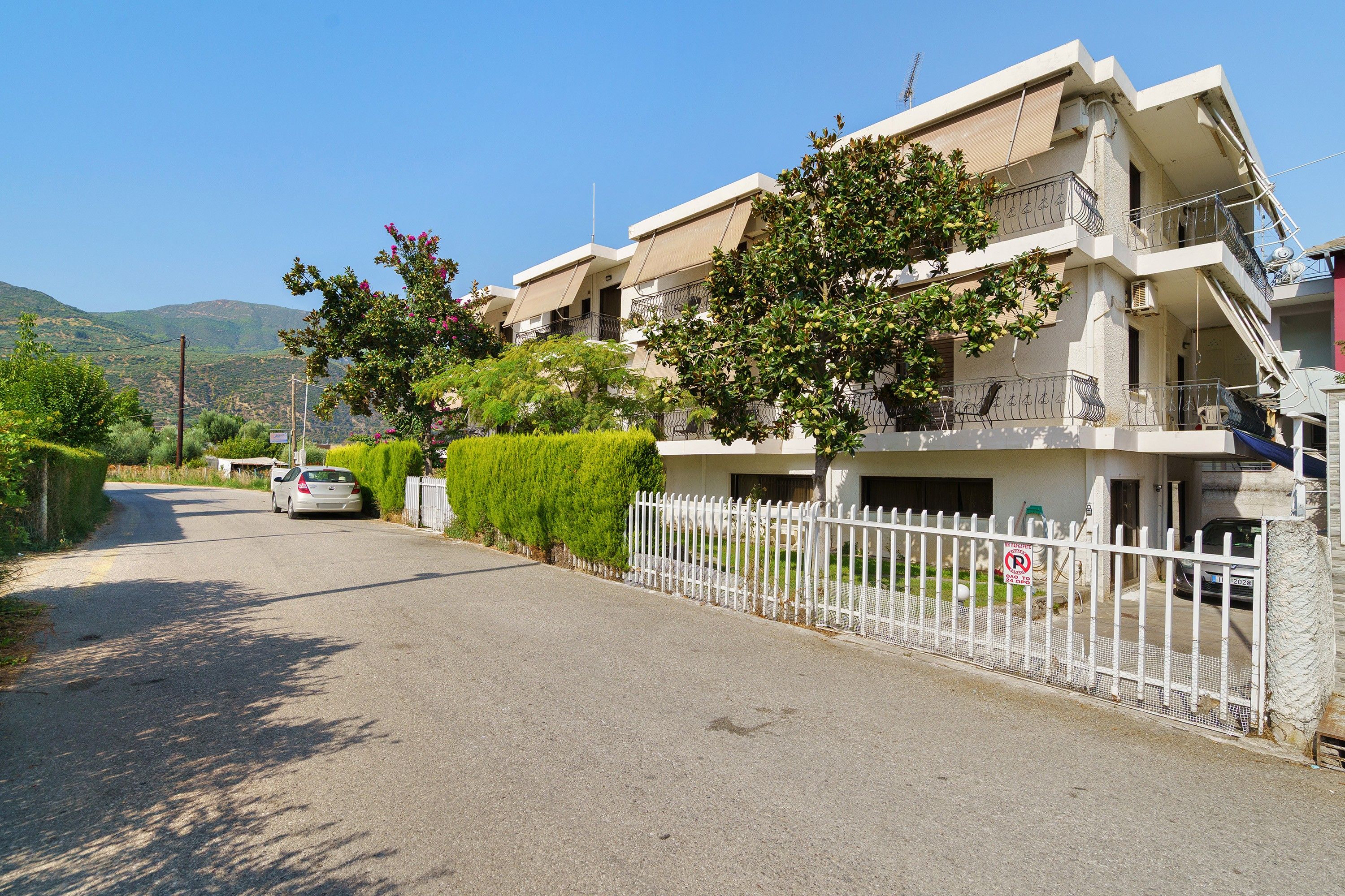 En bostadsgata med en rad tvåvåningshus, ett vitt staket och en parkerad bil.