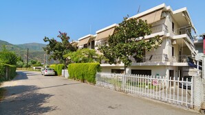 A residential street with a row of two-story houses, a white picket fence, and a parked car. - Rousetis Studio 204 - 200m from the Sea in Aígio (Aigialeia)