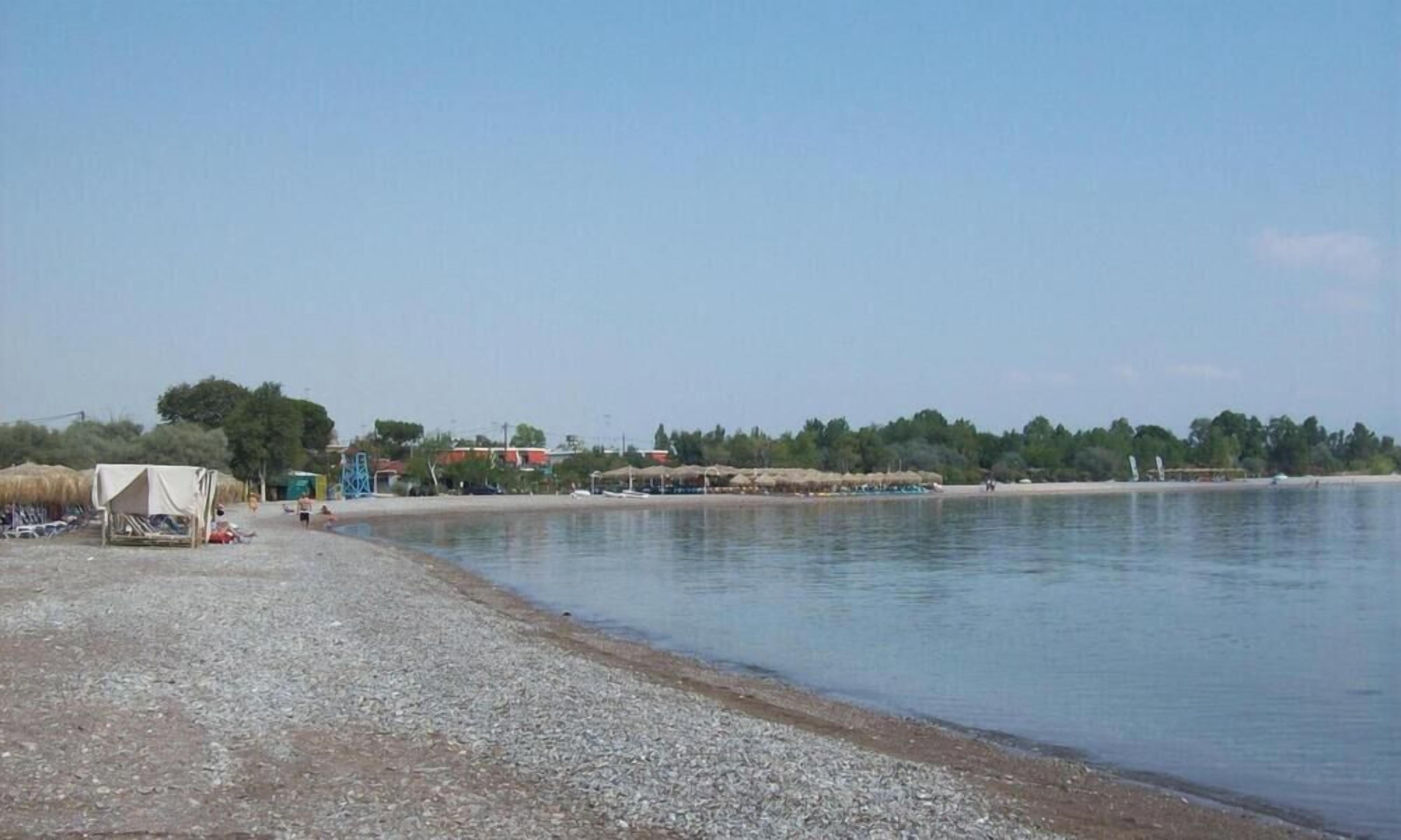 Ein Strand mit Kiesufer, einigen Zelten und einem ruhigen Gewässer.