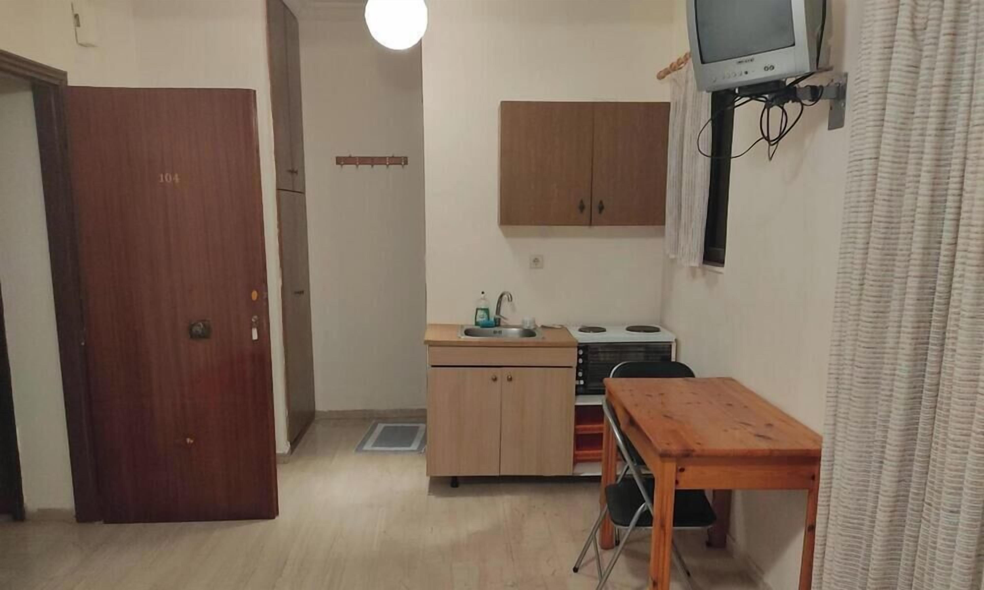 Ett kompakt kök med ett träskåp, ett litet bord och en tv som är monterad på väggen.