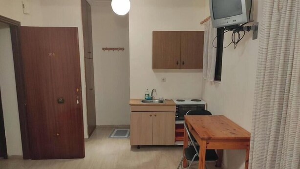 A compact kitchen with a wooden cabinet, a small table, and a television mounted on the wall. - Rousetis Studio 204 - 200m from the Sea in Aígio (Aigialeia)