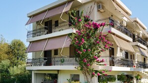 A multi-story residential building with balconies, awnings, and a flowering tree. - Rousetis Studio 204 - 200m from the Sea in Aígio (Aigialeia)