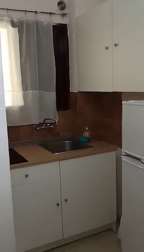 Ett litet kök med en diskho, skåp och ett kylskåp.