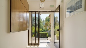 A hallway with a wooden door, a clock, and a view of a garden. - Rousetis Studio 106 - 200m from the Sea in Aígio (Aigialeia)