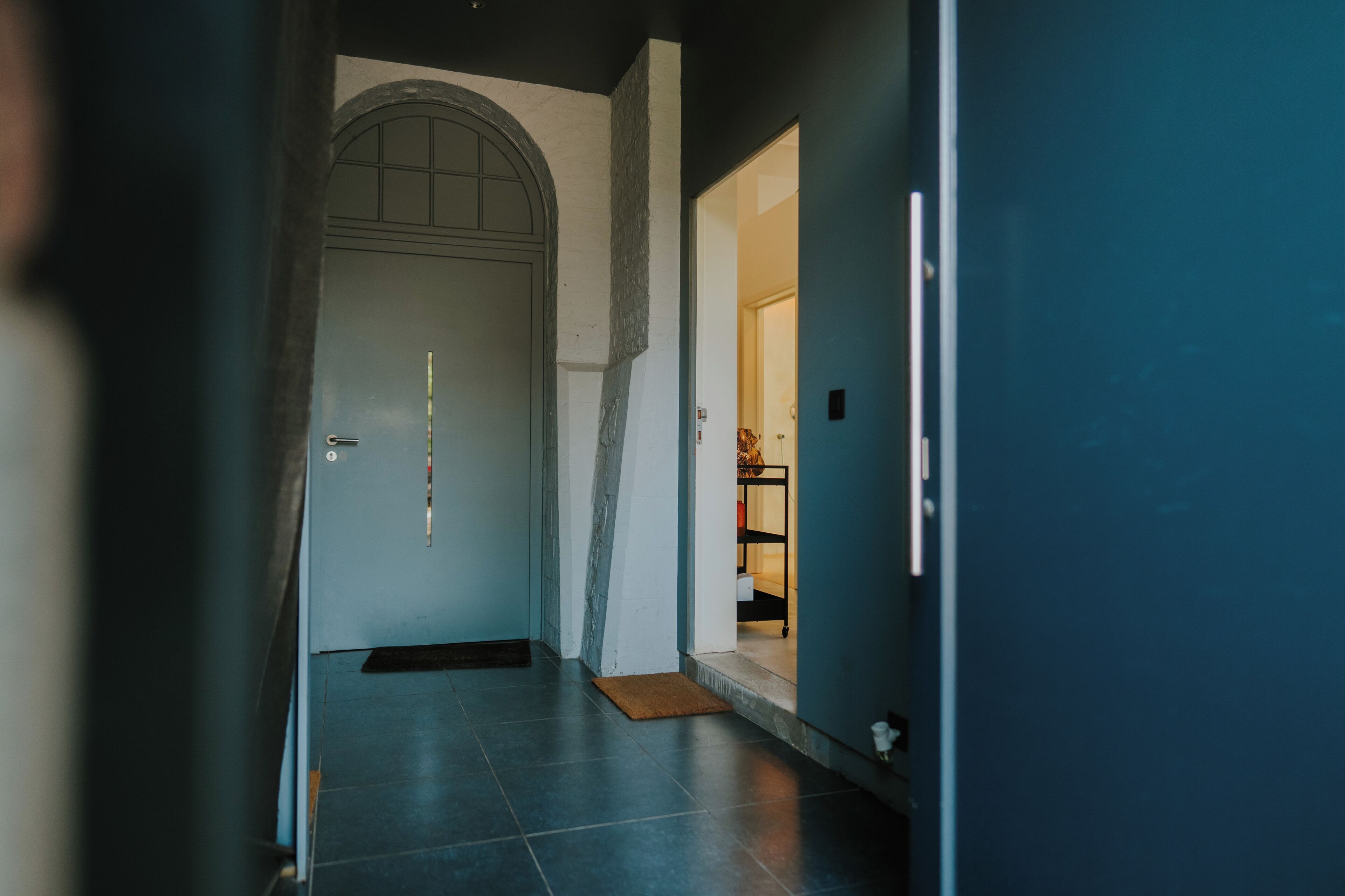 A hallway with a door, a mat, and a shelf with items.