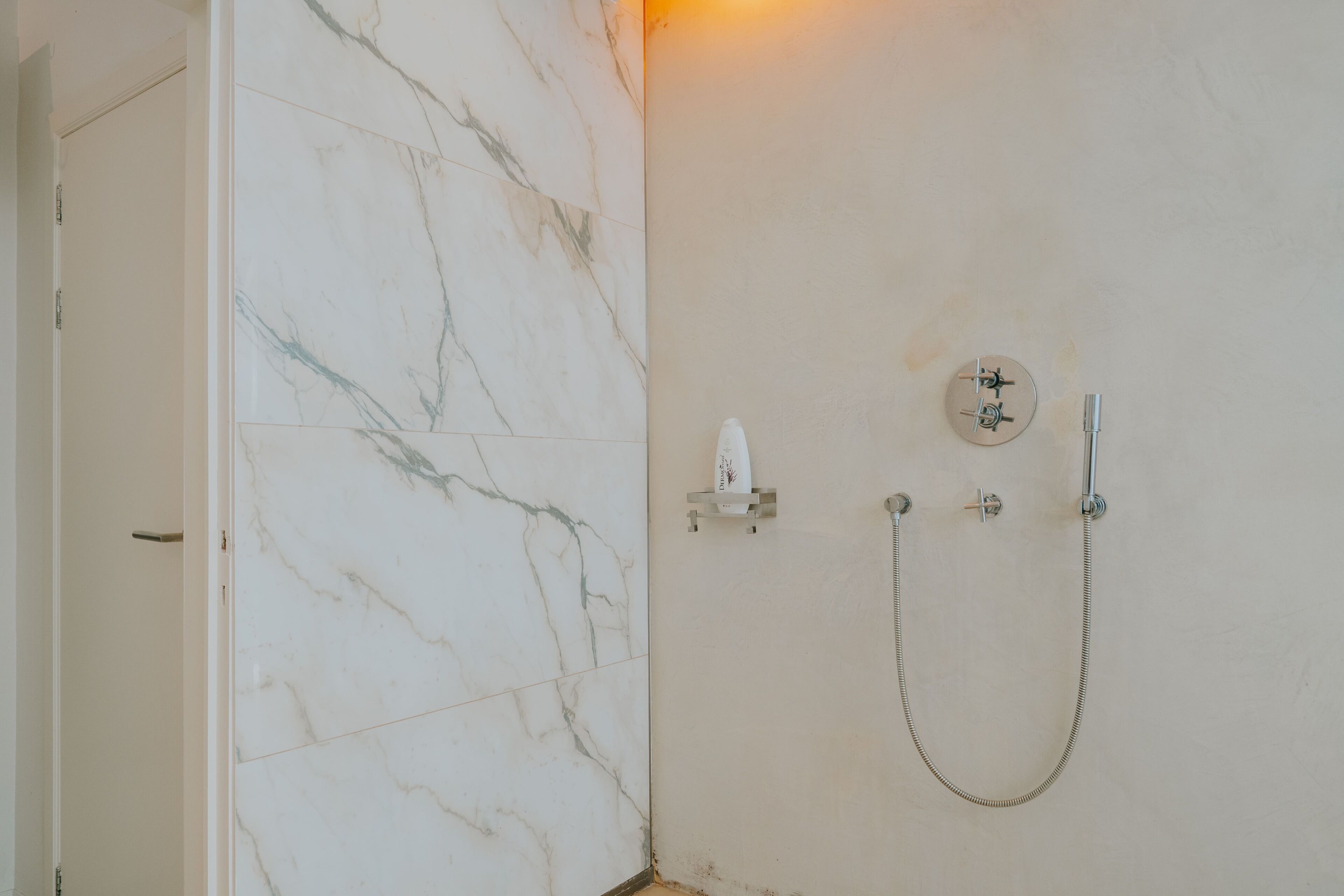 A bathroom with a marble wall, a shower with a handheld showerhead, and a towel rack.