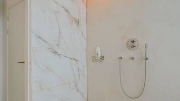 A bathroom with a marble wall, a shower with a handheld showerhead, and a towel rack.