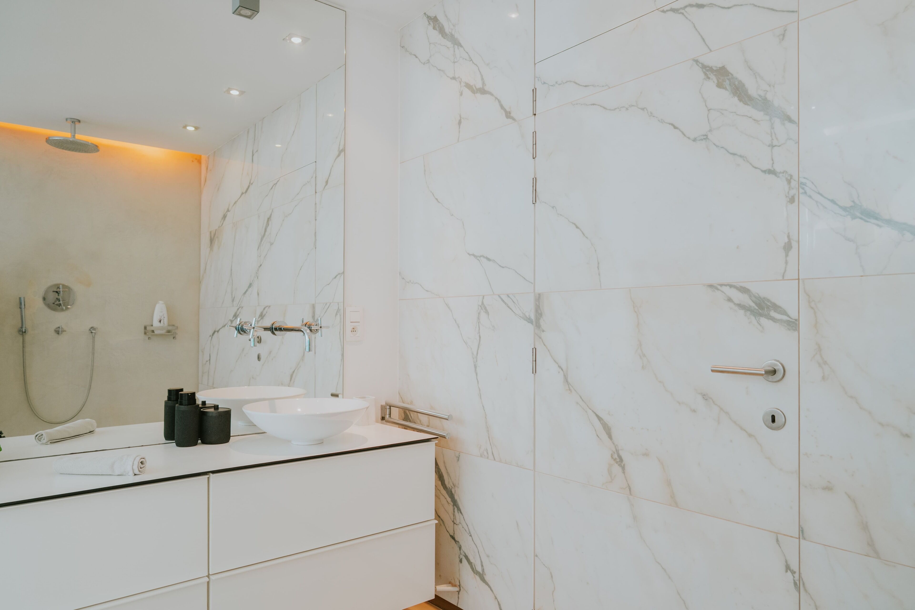 Een moderne badkamer met een wastafel van wit marmer, een grote spiegel en een douche.