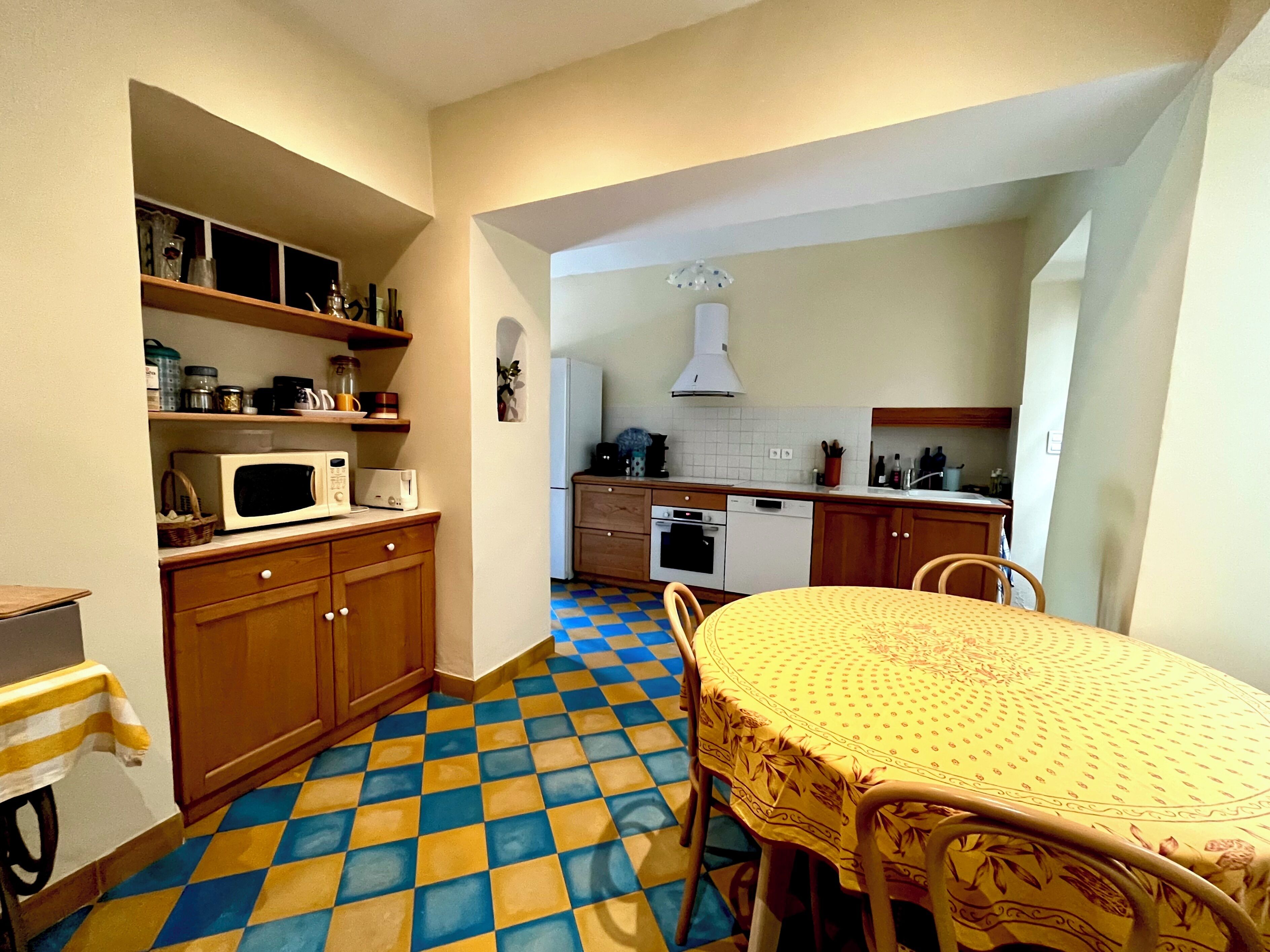 Una cocina compacta con microondas, horno y lavabo, una mesa de comedor con sillas y suelo a cuadros.