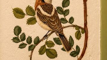 Een muur met een geschilderde vogel die op een tak met bladeren en een bloem zit.