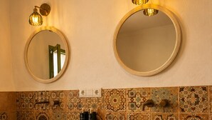Un bagno con due specchi circolari, uno schienale piastrellato color beige e un mobile lavabo in legno con due ampi lavandini in pietra.