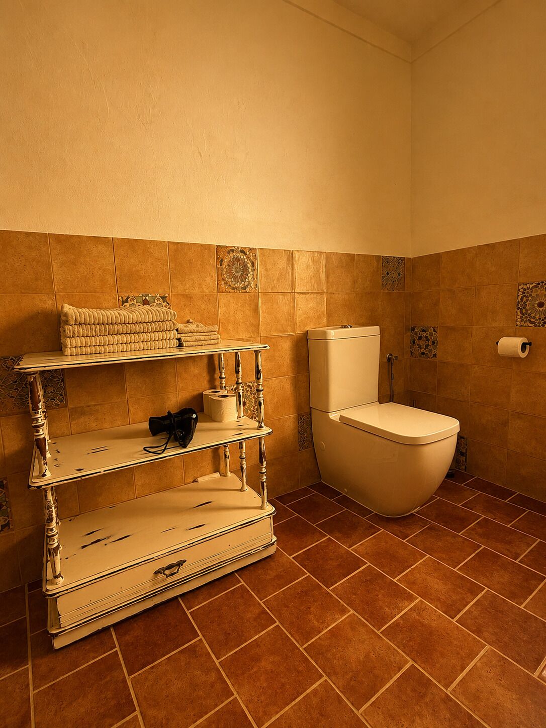 Une salle de bain avec des toilettes, une étagère avec des serviettes et un rouleau de papier toilette.
