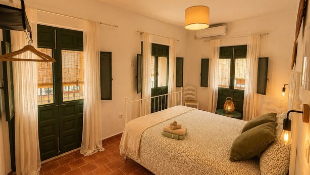 Ein Schlafzimmer mit einem Bett, einem Sessel, einem Kleiderständer und einem Fenster mit Vorhängen.