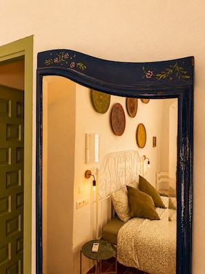 Une chambre à coucher avec un lit, une table de chevet et un miroir orné d’assiettes décoratives accrochées au mur.
