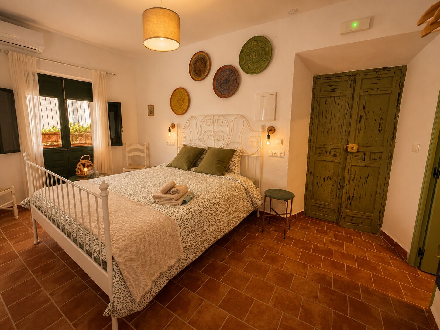 A bedroom with a bed, bedside lamps, a green door, and a wall with decorative plates.