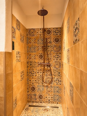 Une douche équipée d’un pommeau de douche à main et d’un mur orné de motifs complexes en carreaux.
