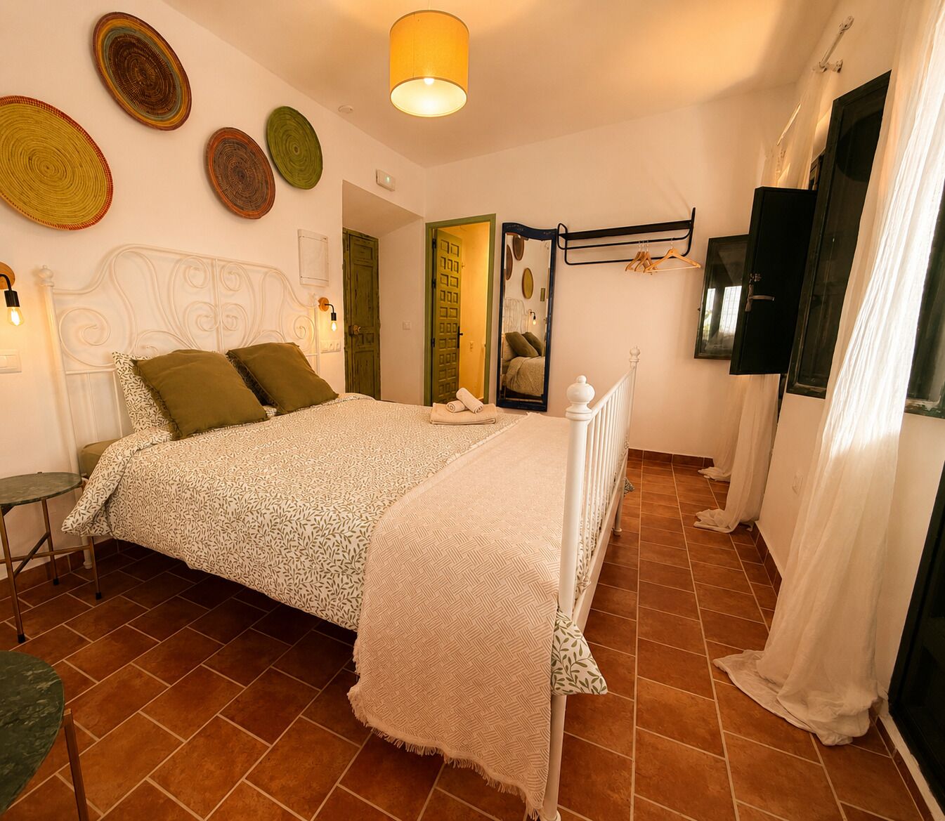 A bedroom with a bed, a bedside table, a hanging light fixture, and a mirror.