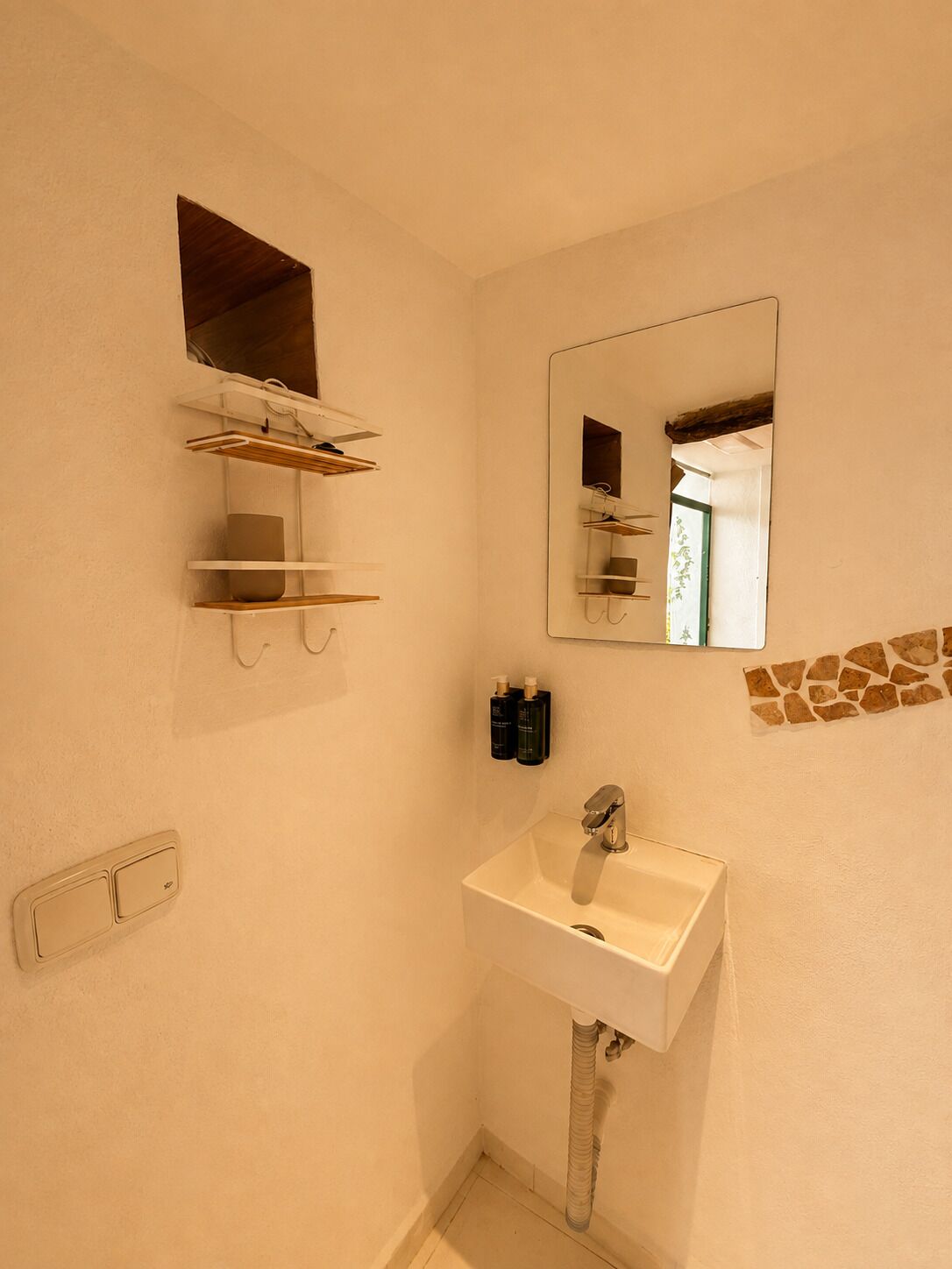 Een badkamer met een witte wastafel, een spiegel en een plank met toiletartikelen.