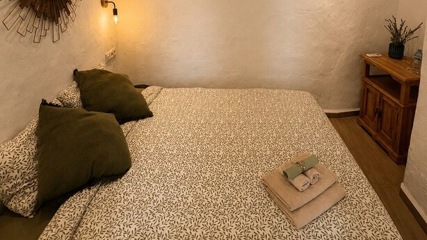 Une chambre à coucher comprenant un lit, des oreillers, un miroir fixé au mur et deux œuvres d’art encadrées.