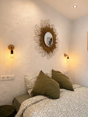 Un dormitorio con una cama, dos luces empotradas, un espejo redondo y un enchufe.