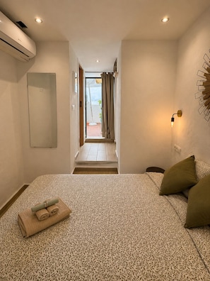 Habitación de hotel con cama, aire acondicionado de pared, puerta que da a un balcón y aplique de luz en la pared.
