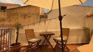Eine Terrasse im Freien mit Tisch, Stühlen, einer Kübelpflanze und einem großen Sonnenschirm.
