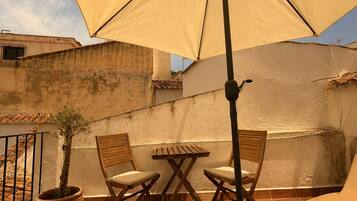 Un patio al aire libre con una mesa, sillas, una planta en maceta y un paraguas grande.
