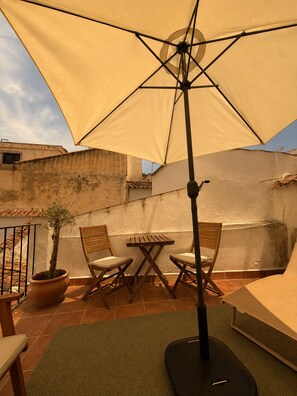 Une terrasse extérieure avec une table et des chaises, une plante en pot et un grand parasol.
