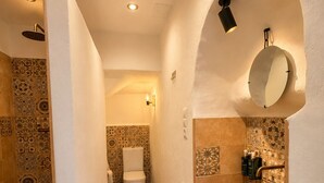 Ein schmales Badezimmer mit gemusterten Fliesen, einer weißen Toilette, einem großen, ovalen Waschbecken und einem Spiegel an der Wand.