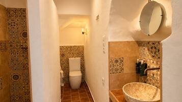 Un baño estrecho con baldosas estampadas, un inodoro blanco, un lavamanos ovalado grande y un espejo en la pared.