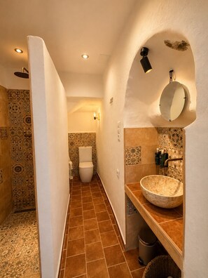 Une petite salle de bain aux carreaux décorés, avec des toilettes blanches, un grand lavabo ovale et un miroir au mur.