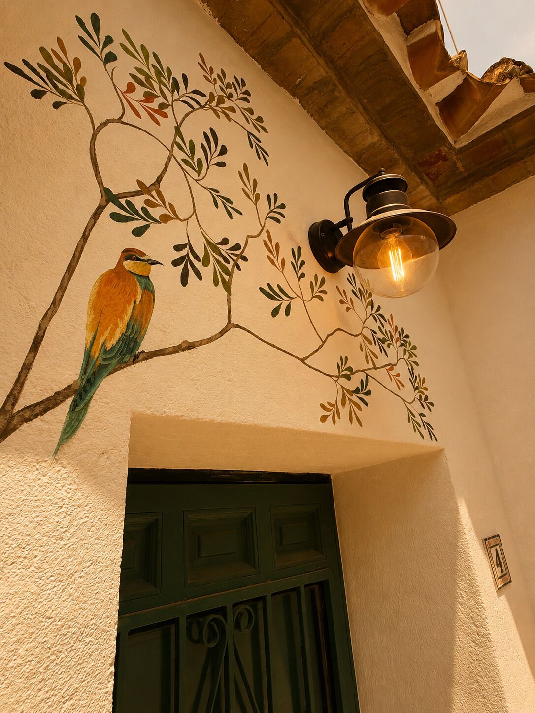 Een muur met een geschilderde tak en een vogel, een groene deur en een hangende lamp.