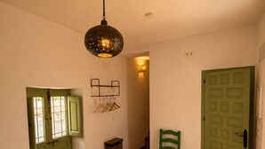 Ein Zimmer mit einem geblümten Bettbezug, einem grünen Sessel, einer grünen Tür, einem Wandhaken für Kleider und einer Pendelleuchte.