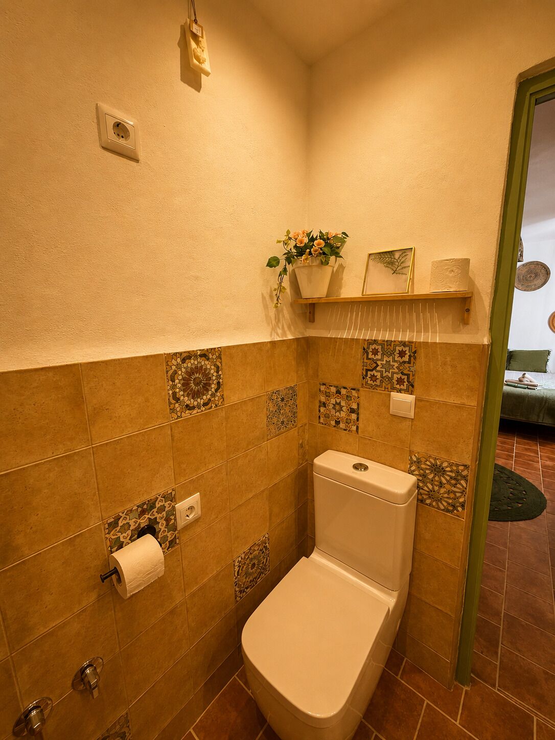 Une salle de bain avec des toilettes, une douche et un lavabo. Une serviette est accrochée au mur et une petite étagère porte une plante.