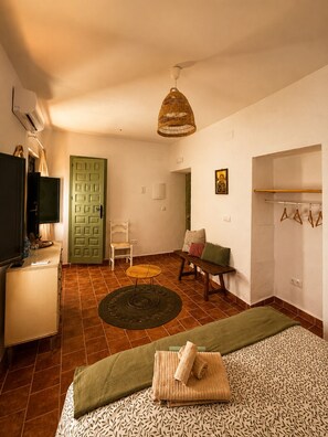Una habitación con cama, una silla, una mesita, un televisor y una puerta verde.