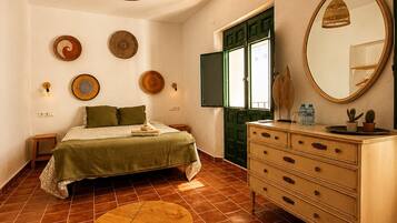 A bedroom with a bed, dresser, mirror, wall art, and a hanging light fixture.