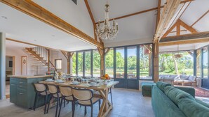 Une salle à manger spacieuse, avec une grande table en bois dressée pour six personnes, entourée de chaises, et une large fenêtre donnant sur l’extérieur.