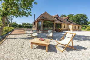 Een houten tuinhuis met pannendak, omgeven door grind en voorzien van twee loungestoelen en een tafel.