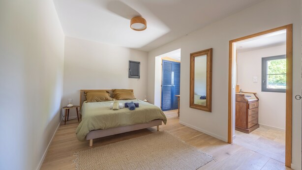 Une chambre à coucher avec un lit, une table de chevet, un miroir et une vue sur l’extérieur.