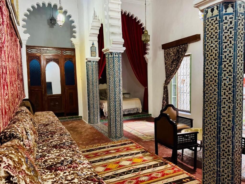 A room with a patterned sofa, a bed with a patterned bedspread, and a chair. There are decorative columns and a patterned wall.